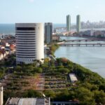 Sede do TRF5 em Recife, edifício cilíndrico branco às margens do Rio Capibaribe, com vista aérea do centro histórico e orla ao fundo