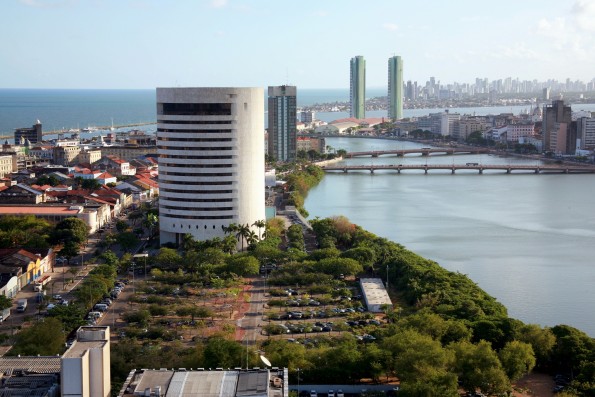 Sede do TRF5 em Recife, edifício cilíndrico branco às margens do Rio Capibaribe, com vista aérea do centro histórico e orla ao fundo