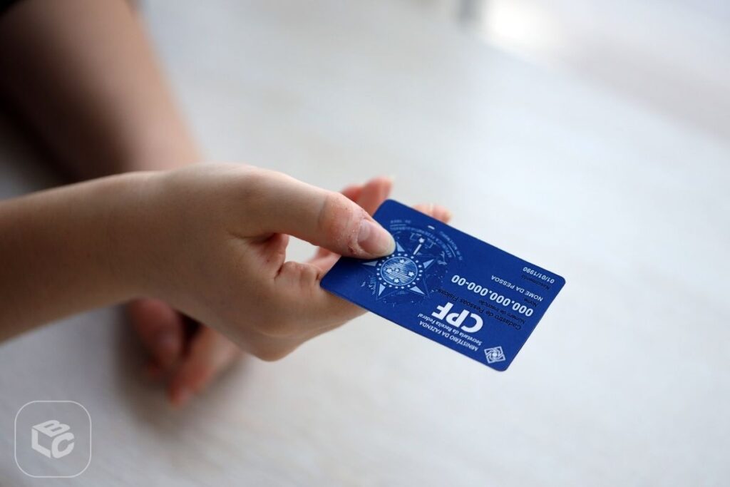 Mão segurando cartão CPF azul com dados visíveis, para consulta RPV TRF5