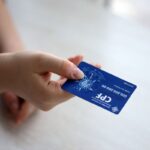 Mão segurando cartão CPF azul com dados visíveis, para consulta RPV TRF5